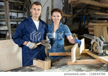 Man and woman employees of carpentry workshop work together, use circular saw, drill Man and woman employees of carpentry workshop work together, use circular saw, drill 116644700