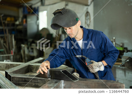 During manufacture of product, man employee works with welding machine 116644760