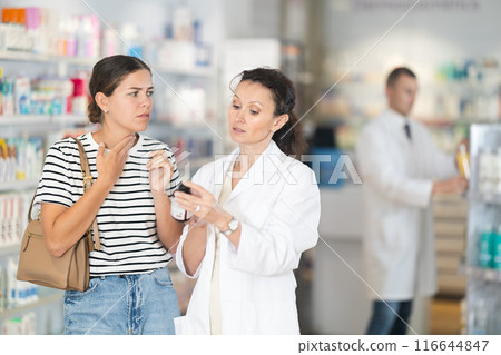 Middle-aged female pharmacist offering medicine to girl suffering from pain 116644847