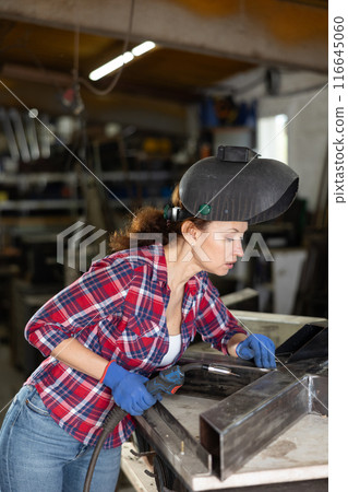 Adult woman welding metal part in workshop Adult woman welding metal part in workshop 116645060