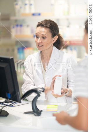 Female pharmacist at cash register scans a QR code and sells medicine to pharmacy visitor. 116645068