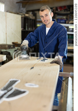 During manufacturing, man employee grinds surface of wooden board, gives smoothness to surface During manufacturing, man employee grinds surface of wooden board, gives smoothness to surface 116645109