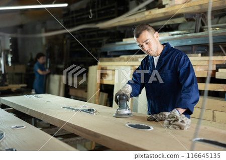 Young man polishing oak plank in workshop 116645135