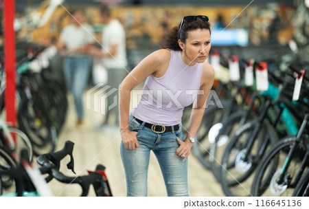 Portrait of positive woman standing in bicycle store and choosing new comfortable bike 116645136