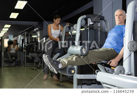 Elderly man trains his legs on machine Elderly man trains his legs on machine 116645239