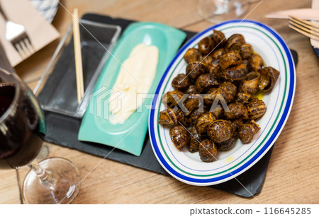 Flavored caracoles(Spanish) snails in shells, served with white sauce and red wine presented in a restaurant 116645285