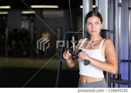 Athletic girl work out muscles of arms and shoulders on rope loop simulator in gym of fitness club 116645292