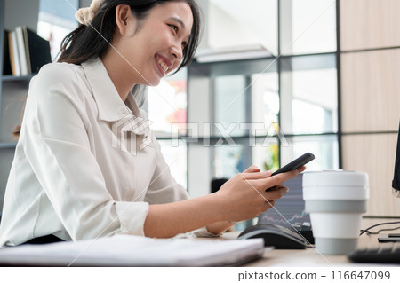 Woman examines stock graphs at office desk using phone 116647099
