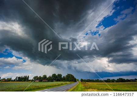 Storm clouds loom over rural landscape, creating a dramatic scene as a car drives down the road Storm clouds loom over rural landscape, creating a dramatic scene as a car drives down the road 116647357