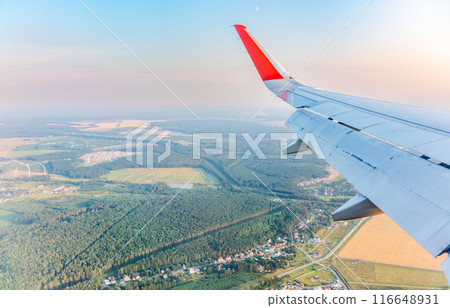 View of airplane wing, blue skies and green land during landing. Airplane window view. View of airplane wing, blue skies and green land during landing. Airplane window view. 116648931