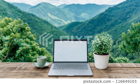 Laptop on wooden table with coffee cup and plant, overlooking beautiful green mountain landscape. Perfect for remote work inspiration. 116649103