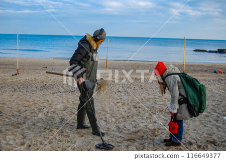 Searching for jewelry on the beach. A treasure hunter and an assistant clean the beach of metal before the season. Searching for jewelry on the beach. A treasure hunter and an assistant clean the beach of metal before the season. 116649377