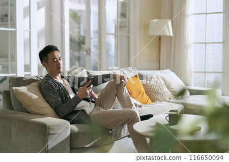 young asian man using mobile phone at home young asian man using mobile phone at home 116650094
