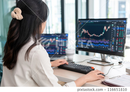 Young woman examines stock graphs at office desk Young woman examines stock graphs at office desk 116651810