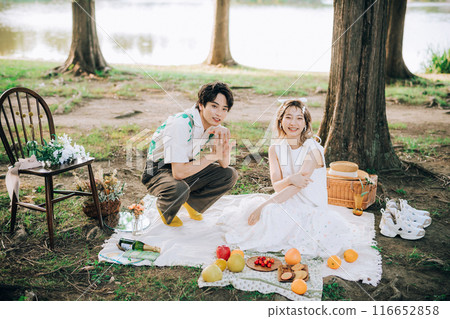 Bride and groom having pre-wedding photos while having a picnic 116652858