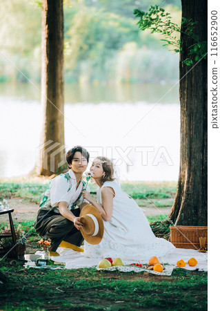 Bride and groom having pre-wedding photos while having a picnic Bride and groom having pre-wedding photos while having a picnic 116652900
