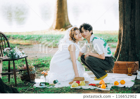 Bride and groom having pre-wedding photos while having a picnic Bride and groom having pre-wedding photos while having a picnic 116652902