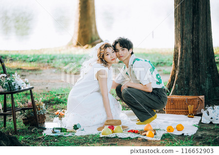 Bride and groom having pre-wedding photos while having a picnic Bride and groom having pre-wedding photos while having a picnic 116652903