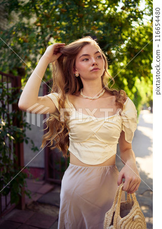 beautiful teenage girl in a silk skirt and a corset in the old money style strolls through the city 116654480