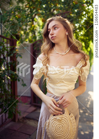 beautiful teenage girl in a silk skirt and a corset in the old money style strolls through the city 116654483