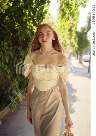 beautiful teenage girl in a silk skirt and a corset in the old money style strolls through the city 116654512
