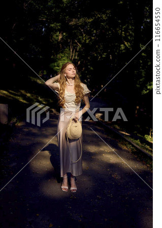 beautiful teenage girl in a silk skirt and a corset in the old money style walks in the park and along the river bank 116654550