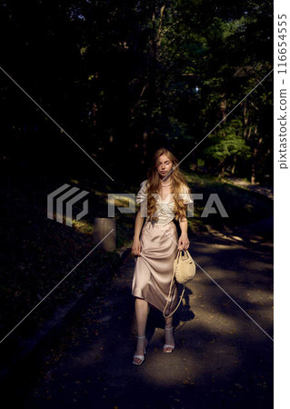 beautiful teenage girl in a silk skirt and a corset in the old money style walks in the park and along the river bank 116654555
