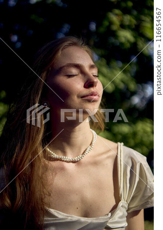 beautiful teenage girl in a silk skirt and a corset in the old money style walks in the park and along the river bank 116654567