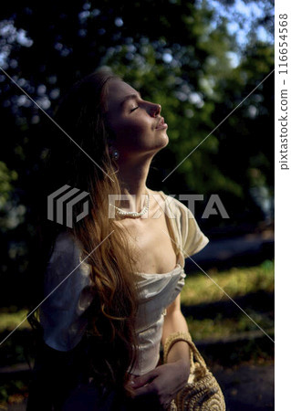 beautiful teenage girl in a silk skirt and a corset in the old money style walks in the park and along the river bank 116654568
