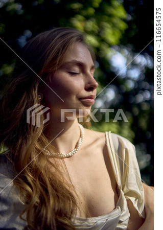 beautiful teenage girl in a silk skirt and a corset in the old money style walks in the park and along the river bank 116654575