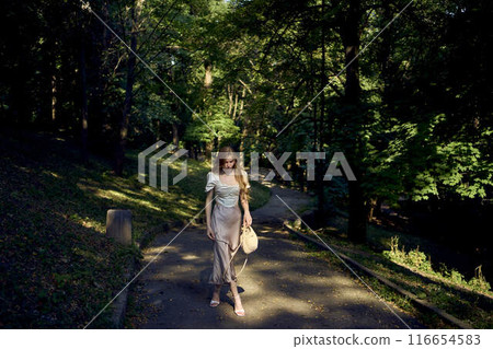 beautiful teenage girl in a silk skirt and a corset in the old money style walks in the park and along the river bank 116654583