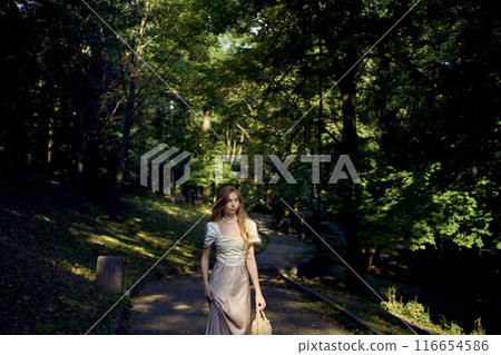 beautiful teenage girl in a silk skirt and a corset in the old money style walks in the park and along the river bank 116654586