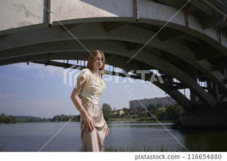 beautiful teenage girl in a silk skirt and corset in the old money style. Fashion photoshoot under the bridge. beautiful teenage girl in a silk skirt and corset in the old money style. Fashion photoshoot under the bridge. 116654880