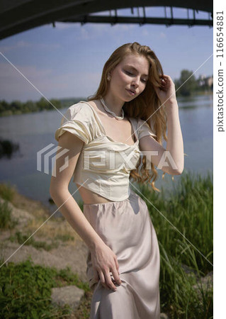 beautiful teenage girl in a silk skirt and corset in the old money style. Fashion photoshoot under the bridge. beautiful teenage girl in a silk skirt and corset in the old money style. Fashion photoshoot under the bridge. 116654881
