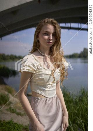 beautiful teenage girl in a silk skirt and corset in the old money style. Fashion photoshoot under the bridge. beautiful teenage girl in a silk skirt and corset in the old money style. Fashion photoshoot under the bridge. 116654882