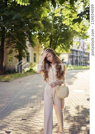 a beautiful teenage girl in a peach fuzz suit with a waistcoat, in the old money style  walks through the morning city 116654899