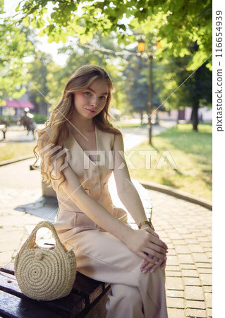 a beautiful teenage girl in a peach fuzz suit with a waistcoat, in the old money style  walks through the morning city 116654939