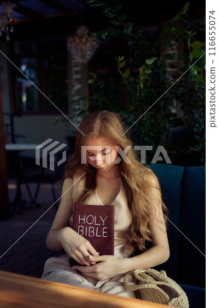 beautiful teenage girl in a peach fluffy suit with a waistcoat in the old money  style reads the Holy Bible and prays 116655074