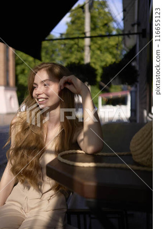 a  beautiful teenage girl in a peach fuzz suit with a waistcoat in the old money  style sits at the bar outside 116655123