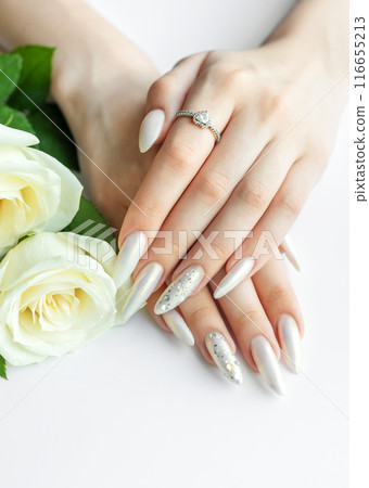 Female Hands on a white background with beautiful pearl manicure and white roses. Female Hands on a white background with beautiful pearl manicure and white roses. 116655213