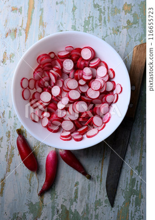 Thin radish slices in a wooden plate with knife Thin radish slices in a wooden plate with knife 116655723