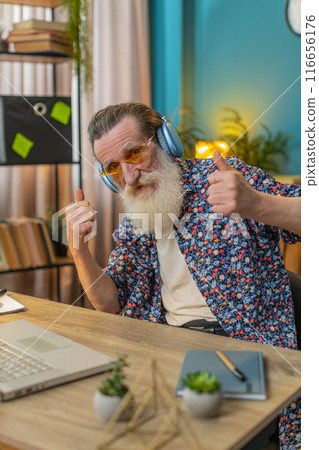 Happy senior man listening music through wireless headphones relaxing taking a break with laptop Happy senior man listening music through wireless headphones relaxing taking a break with laptop 116656176