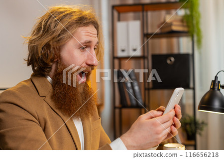 Happy amazed businessman working on smartphone shocked by victory game lottery jackpot winning 116656218