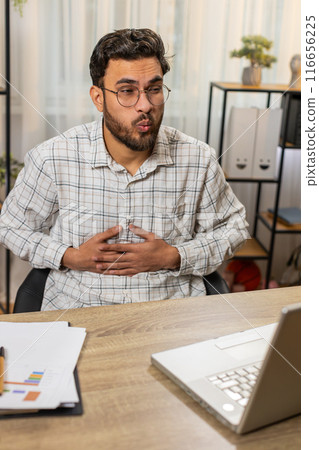 Upset Indian businessman freelancer touching stomach and experiencing discomfort sharp pain 116656225