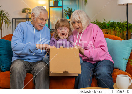 Happy excited grandparents and granddaughter girl opening cardboard box unpack good parcel at home 116656238
