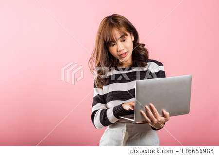 Portrait of happy Asian beautiful young woman confident smiling face holding using laptop computer looking to camera, studio shot isolated on pink background with copy space, notebook computer 116656983