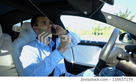 Male entrepreneur speaking by smartphone during riding on electrical auto with autopilot at urban road. Confident businessman talking on phone while riding an autonomous self driving electric car 116657179