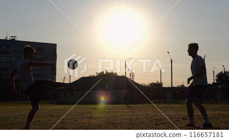 Silhouette of professional footballers kicking soccer ball with their heads on stadium at sunset. Two sportsmen showing tricks with ball while passing it to each other at field. Freestyle football Silhouette of professional footballers kicking soccer ball with their heads on stadium at sunset. Two sportsmen showing tricks with ball while passing it to each other at field. Freestyle football 116657181
