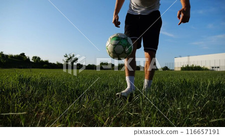 Sportsman juggling soccer ball on stadium at sunny day. Young man kicking ball at green field. Professional footballer practicing tricks at meadow with sunlight at background. Freestyle football. Sportsman juggling soccer ball on stadium at sunny day. Young man kicking ball at green field. Professional footballer practicing tricks at meadow with sunlight at background. Freestyle football. 116657191