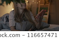 Joyful young lady taking selfie with smartphone camera posing lying in bed in bedroom in evening. Photography and modern lifestyle concept. 116657471